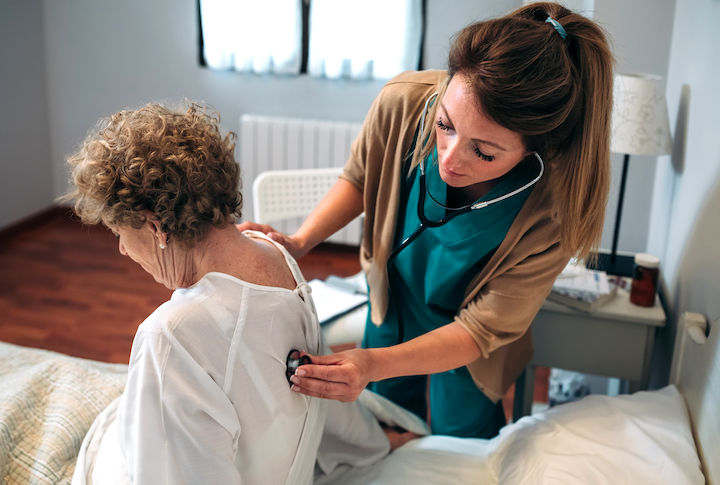 Female caregiver auscultating senior woman at home
