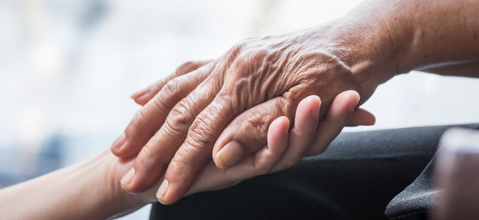 an elderly hand in the hand of a younger caregiver