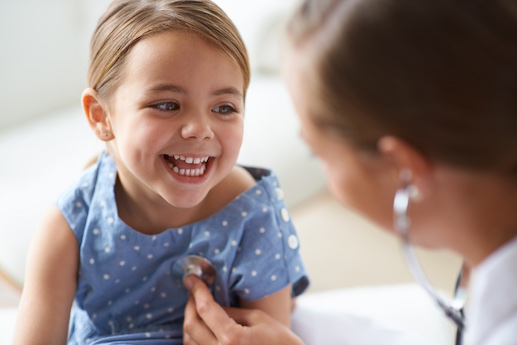 Child smiling at physician while physician listens to her heart.