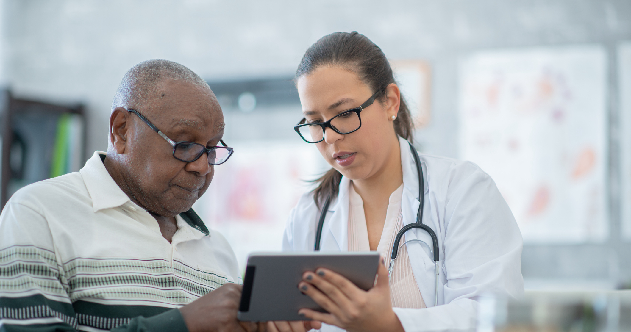 A Hispanic female doctor sits next to her patient at her office to discuss some test results. Her patient is a senior African American male.