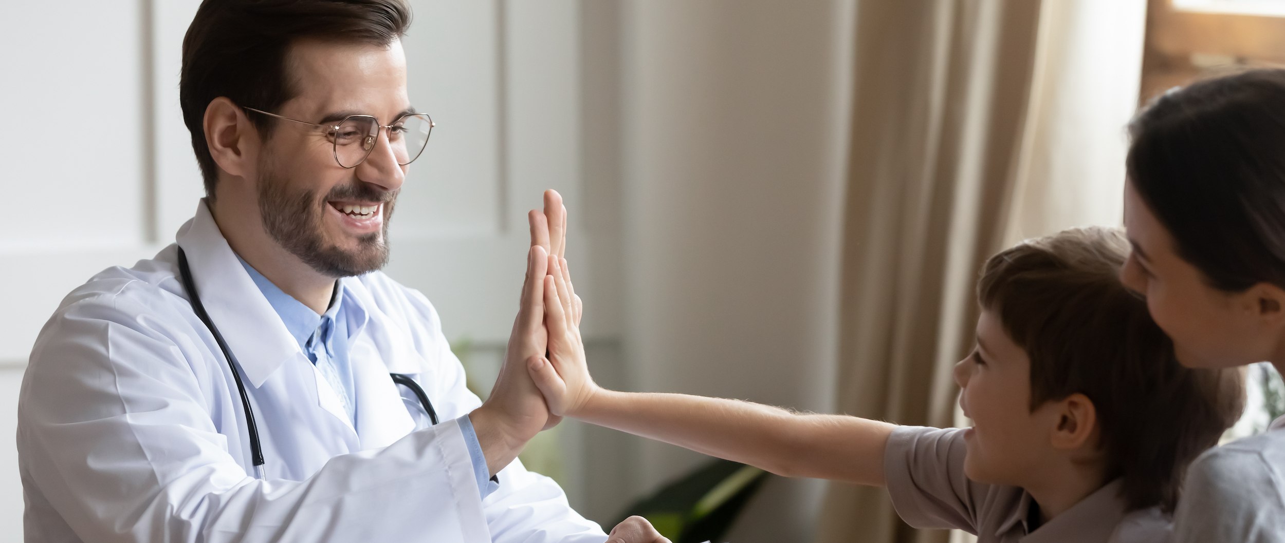 Doctor high-fiving young patient with mother in the background.