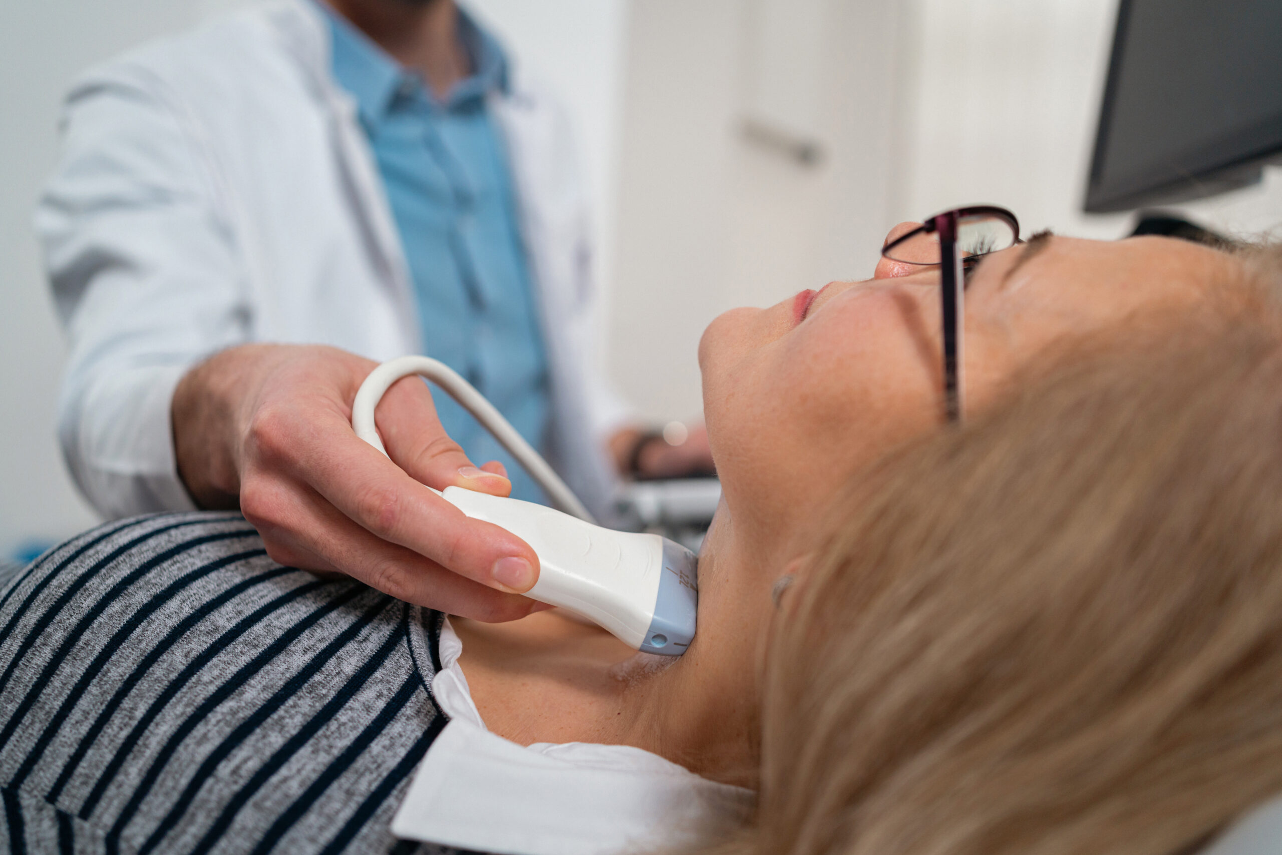 Close-up of an unrecognizable male Caucasian doctor, an endocrinologist doing the ultrasound of the thyroid gland on a senior female patient at the medical clinic
