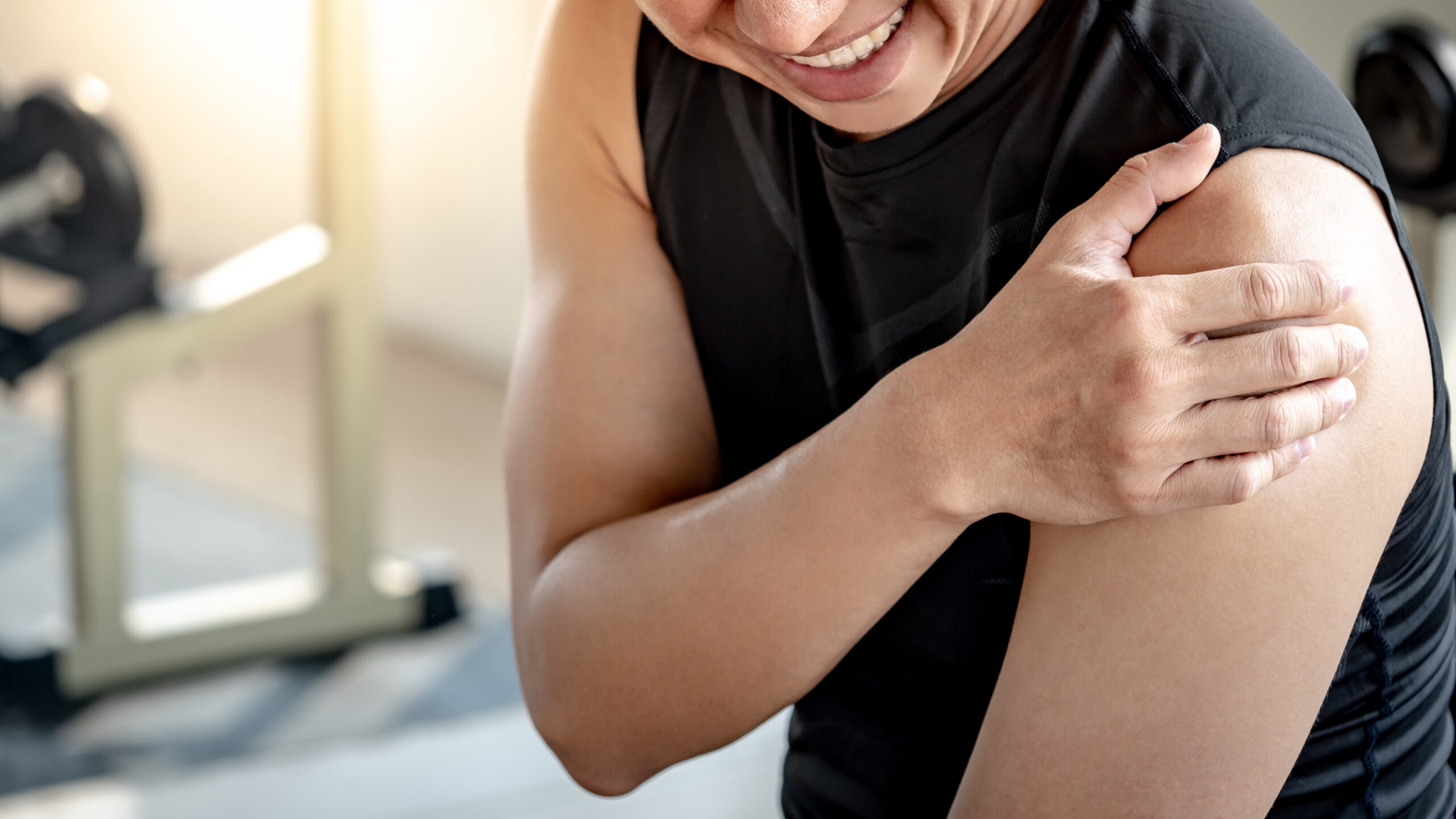 Sportive man feeling shoulder pain after doing weight training exercise in fitness gym. Male athlete suffering from acute arm joint inflammation symptom. Sport injury concept. West tn healthcare